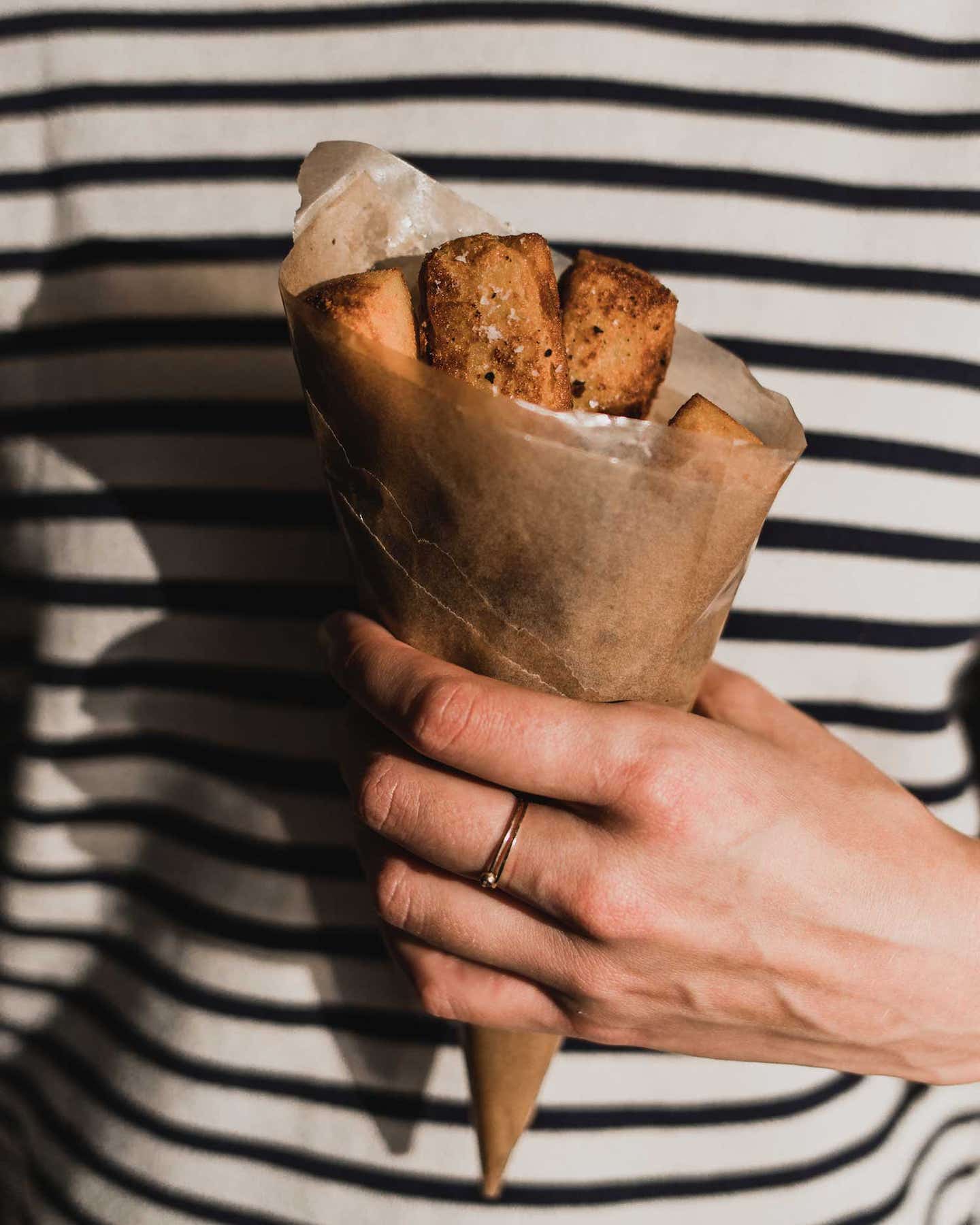 A woman's hand holding a paper cone of panisses.